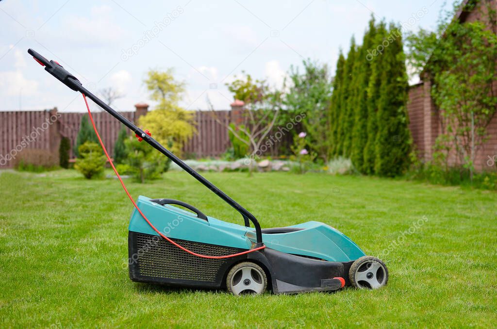 Close up of electrical lawn mower in the garden with freshly cut green grass. Gardening concept.