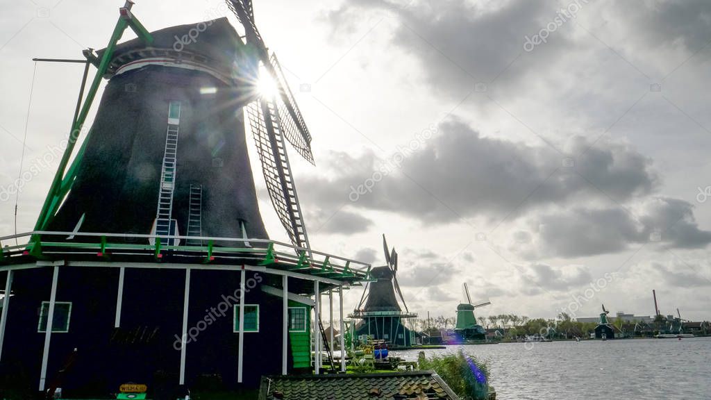 sun behind several windmills at zaanse schans near amsterdam