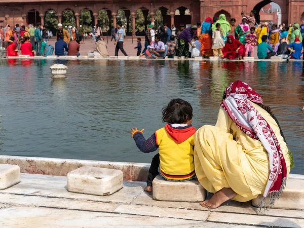 Mulher em sari amarelo lava seu filho sentado na mesquita jama masjid em delhi — Fotografia de Stock