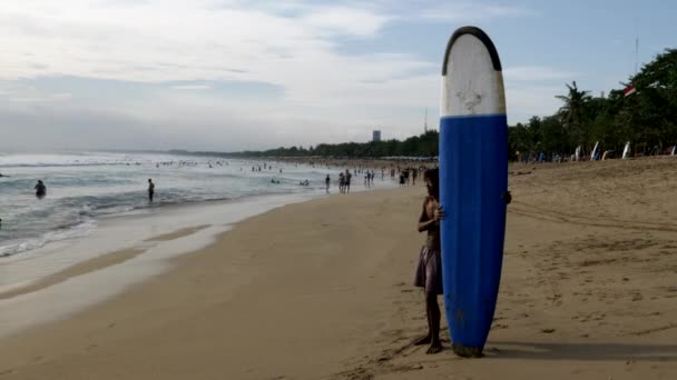 KUTA, INDONESIA - czerwiec, 15, 2017: plażowicz z longboardem obserwuje surfing w kuta, Bali — Wideo stockowe