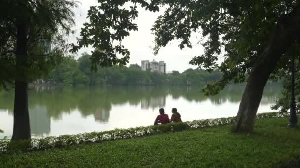 Bred bild av ett ungt par sitta vid hoan kiem sjön — Stockvideo