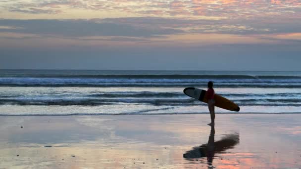 KUTA, INDONESIA - 15 GIUGNO 2017: una ragazza con il longboard guarda il surf al tramonto sulla spiaggia di Kuta — Video Stock