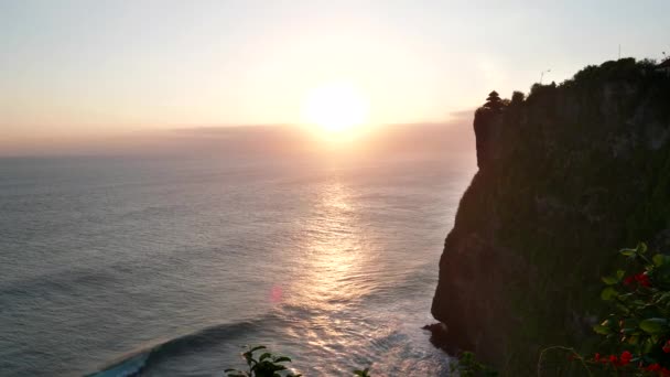 Uluwatu temple with the sun setting in the background and breaking waves at bali — Stock Video