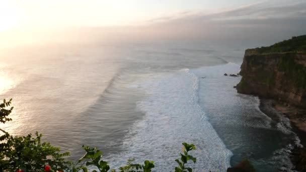 Uluwatu templo al atardecer con el sol brillando en romper las olas en Bali — Vídeos de Stock