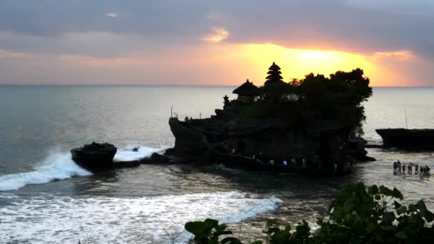 Туристы, выходящие посетить пещеру Танах лот храм на закате на Бали — стоковое видео
