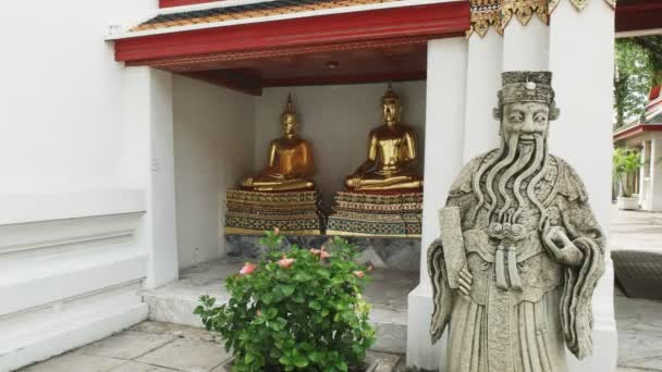Een stenen Chinees standbeeld en twee vergulde Boeddhabeelden bij wat pho tempel in bangkok — Stockvideo
