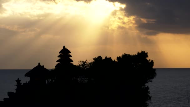 Sun rays above a silhouetted tanah lot temple on bali — Stock Video