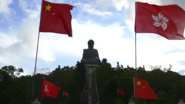 En silhuett solbränd tian buddha staty inramad av kinesiska och hong kong flaggor på lantau ön i hong kong — Stockvideo