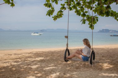 Salıncakta Cennet Adası tropik sahilde oturan kız. Müzik.