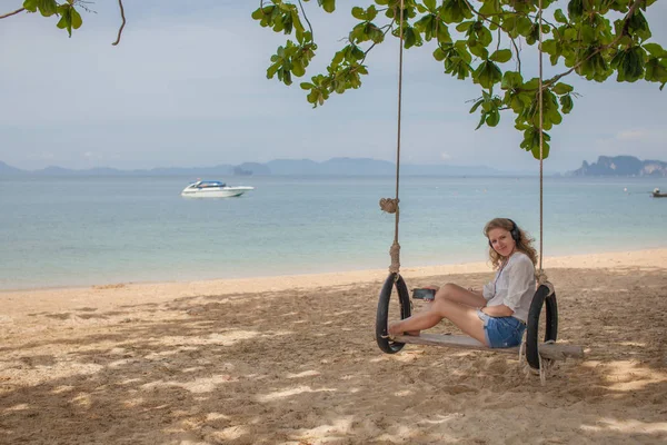 Girl sitting on the swing on the tropical beach, paradise island. Listening to music.