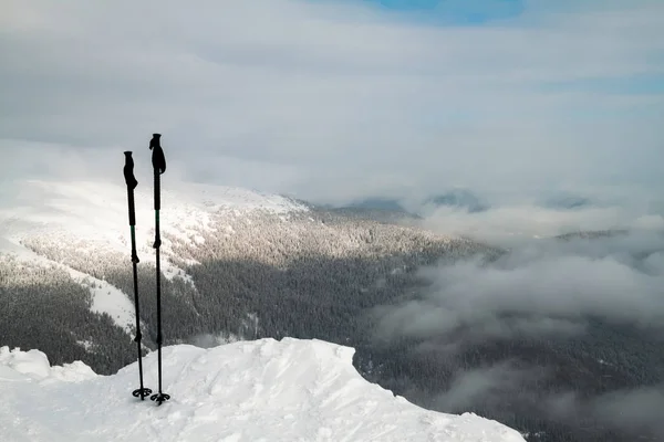 Two ski poles on the top of snowy mountain. Snow covered mountains landscape on the background.