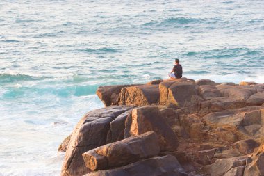 Denizde bir kayanın üzerinde meditasyon yapan adam.