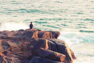 Denizde bir kayanın üzerinde meditasyon yapan adam.