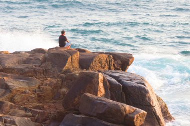 Denizde bir kayanın üzerinde meditasyon yapan adam.