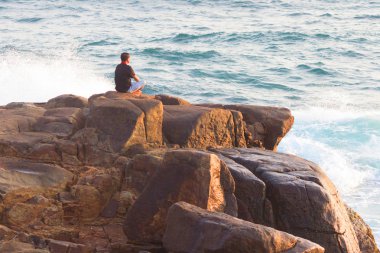 Denizde bir kayanın üzerinde meditasyon yapan adam.