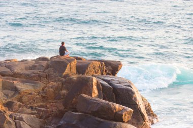 Denizde bir kayanın üzerinde meditasyon yapan adam.