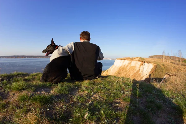 Visão traseira de um homem e um cão sentados na praia — Fotografia de Stock