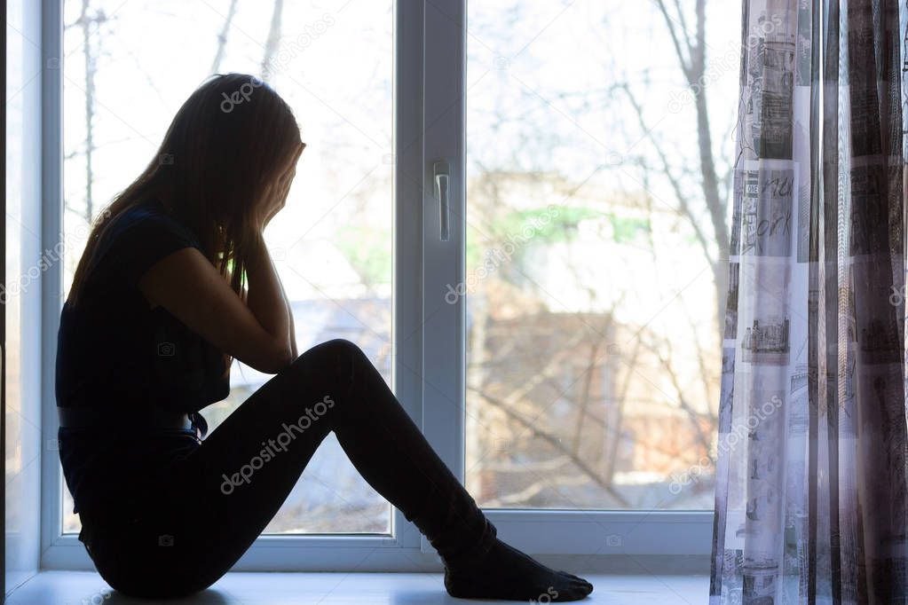 Woman sitting on windowsill, crying
