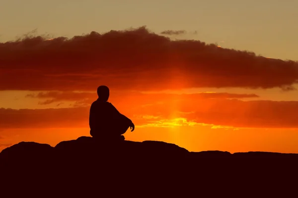 Guy meditando al atardecer sentado en una roca junto al mar —  Fotos de Stock