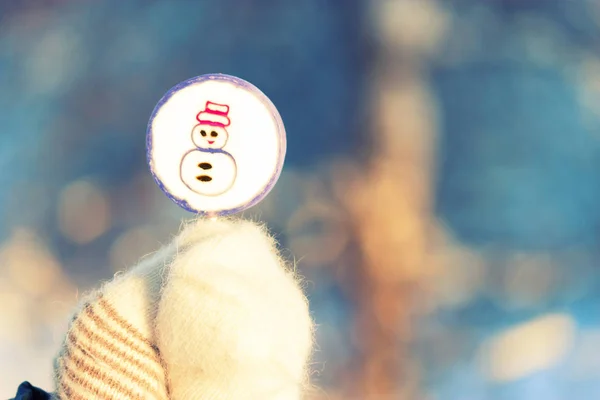 Lollipop på pinne i handen i vanten. snö bakgrunden — Stockfoto