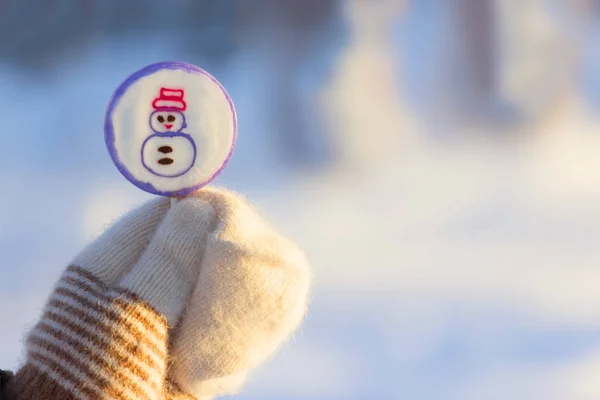 Lollipop på pinne i handen i vanten. snö bakgrunden — Stockfoto