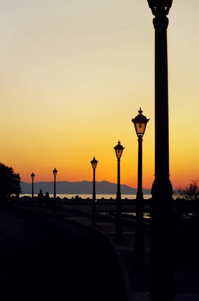 Silhouette of street lights during beautiful sunset. A couple walking by embankment — Stock Photo, Image