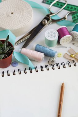 Boş notepad ile kalem iş parçacığı ve iğneleri, iğne, yüksük ve mezura gibi temel dikiş araçları makaralar ile çevrili. Kopya alanı