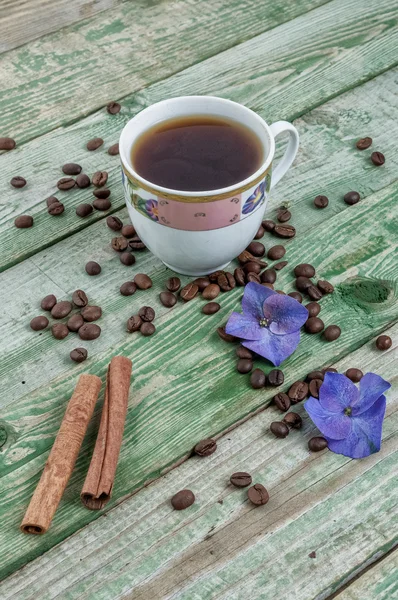 Palitos de canela, granos de café, flor púrpura y café taza sobre fondo verde rústico viejo — Foto de Stock