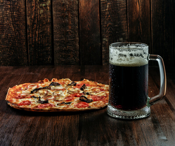 Beer mug and pizza on dark wood background