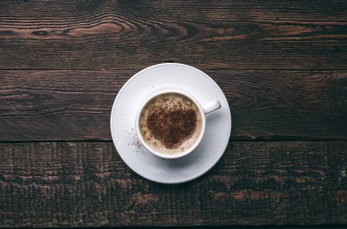 Kalp şeklinde koyu ahşap arka plan üzerinde beyaz kahve fincanı