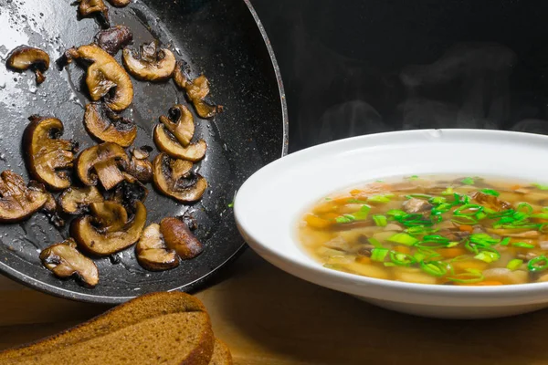 Deliciosa sopa quente na tigela com cogumelos e verduras, e frigideira com cogumelo — Fotografia de Stock