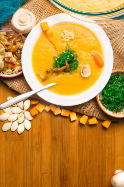 cam sıcak balkabağı çorbası pan ve beyaz plaka mini havuç, kabak çekirdeği, dekore edilmiş, mantar, agaric ve yeşil yosun ahşap tahta üzerinde tatlım. Vegan.