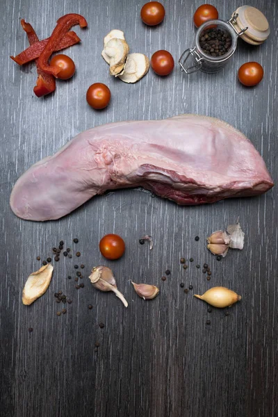 Carne cruda o lengua de cerdo con verduras- apio, pimienta, ajo, cebolla, se encuentra en una tabla de cortar, sobre un fondo negro primer plano —  Fotos de Stock