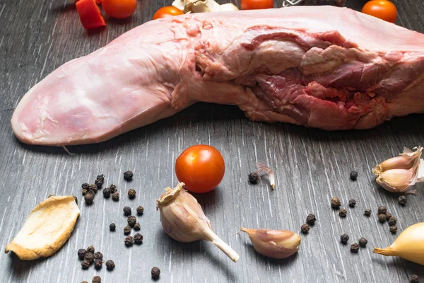 Carne crua ou língua de porco com vegetais- aipo, pimenta, alho, cebola, encontra-se em uma tábua de corte, em um fundo preto close-up — Fotografia de Stock