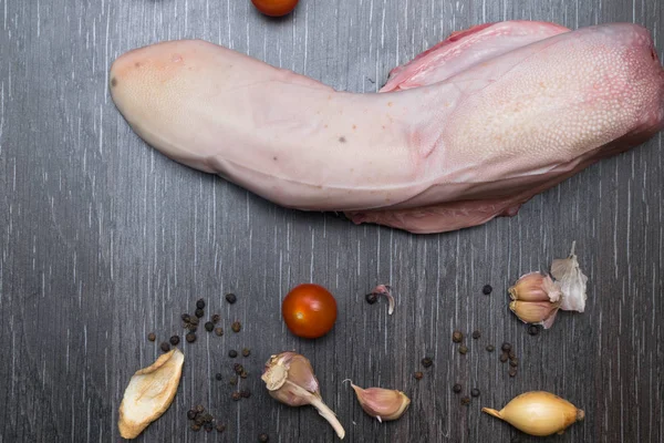 Lengua cruda, de res o de cerdo con verduras se encuentra en una tabla de cortar, sobre un fondo negro primer plano —  Fotos de Stock