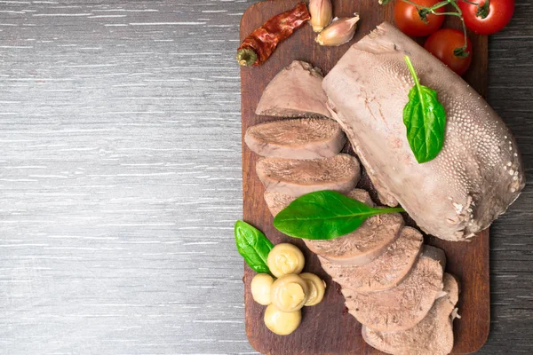 Boiled beef, pork tongue with cherry tomatoes, mushrooms, basil leaf, studio shot, isolated on wood background. Top view