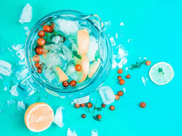 Menyegarkan air lemon dalam kendi kaca dengan es batu pada latar belakang biru — Stok Foto