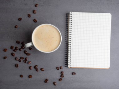 Sabah işyerinde bir fincan kahve, kahve çekirdeği ve not defteri var. Minimalizm kavramı