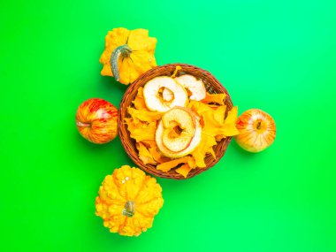 Kurutulmuş meyve ve sebzeler elma dilimleri, yeşil arka planda kahverengi hasır sepetin içindeki balkabağı. Seçici odak.