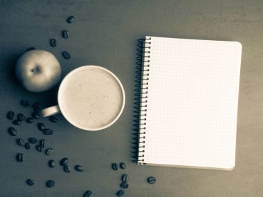 Beyaz not defteri, bir fincan kahve, gri masada elma.