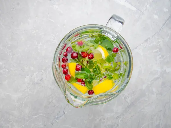 광천수, 레몬 조각, 박하 잎, 대리석 테이블에 크랜 베리가 있는 유리병. 식생활을 위한 음료. 선택적 초점 — 스톡 사진