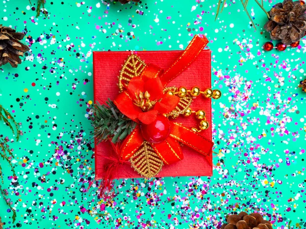 Red gift box with red decoration on turquoise background with colorful glitter, cones. Holiday concept. Topo view — Stock Photo, Image