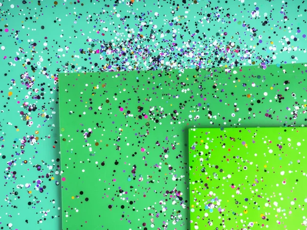 Paper sheets in mixed green colors with holographic foil confetti. Trendy mint and green abstract duo tone background design. Place for text. Main trend and simple holiday concept. Top view