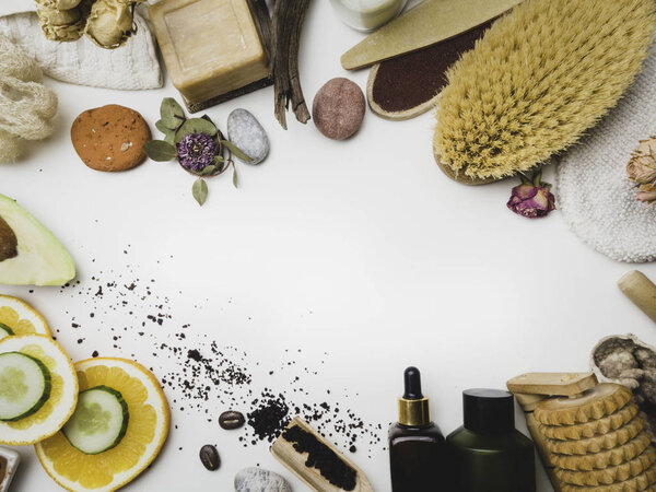 Концепция спа и ухода за кожей на белом фоне. Пространство для текста. Вид сверху. Скраб для тела кофе с натуральными ингредиентами, огурец и апельсин, мыло, сыворотка, масло, камни, массажный инструмент
