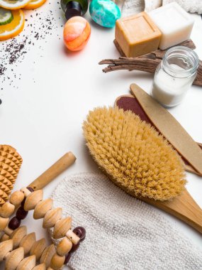 Beyaz arka planda kaplıca ve cilt bakımı konsepti. Mesaj için yer var. Üst Manzara. Doğal malzemeli vücut kahvesi fırçası, salatalık ve portakal dilimleri, sabun, serum, yağ, taş, masaj aleti.