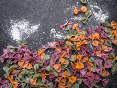 Gri mermer arka planda ev yapımı İtalyan makarnası. Farklı renkte papyon tagliatelle, farfalle makarna. Üst Manzara. Seçici odak.