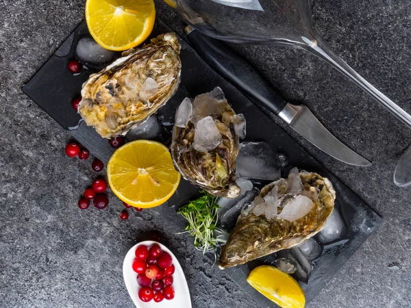 Verse oesters in ijs met citroen, veenbessen, glas voor wijn of champagne, mes over stenen tafel, close up — Stockfoto