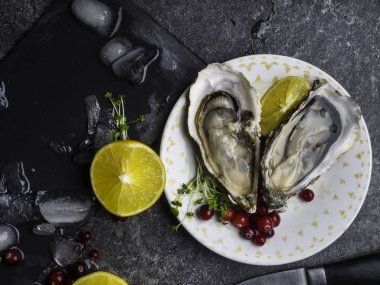 İstiridye kalbi tabakta limon, kızılcık, mikro yeşillik, bıçak, mermer kabuk şeklinde.