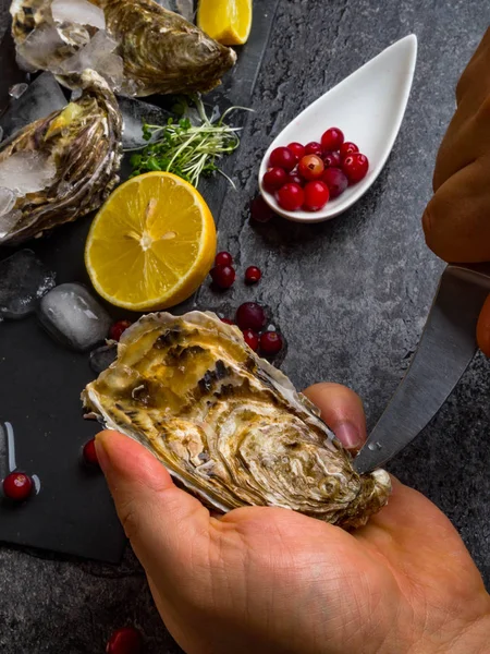 Un hombre que arroja ostras frescas con sus propias manos en la mesa de piedra, rodajas de limón, micro verdes, hielo, arándanos en la mesa — Foto de Stock