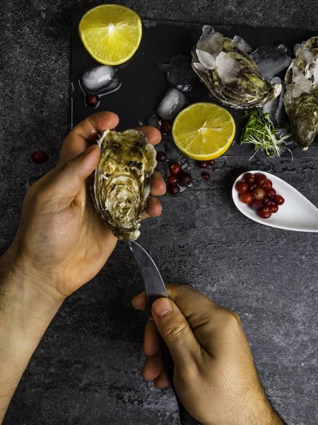 Un hombre que arroja ostras frescas con sus propias manos en la mesa de piedra, rodajas de limón, micro verdes, hielo, arándanos en la mesa — Foto de Stock